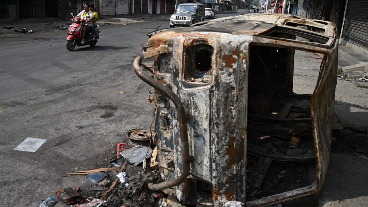 A motorist rides past a burnt vehicle on a street in Churachandpur in violence hit areas of of Manipur where Kukis and Meitis have clashed. Credit: AFP Photo