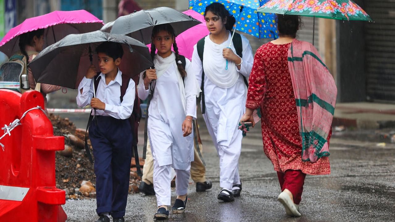 Students walk down a road amid rainfall, in Jammu. Credit: PTI Photo