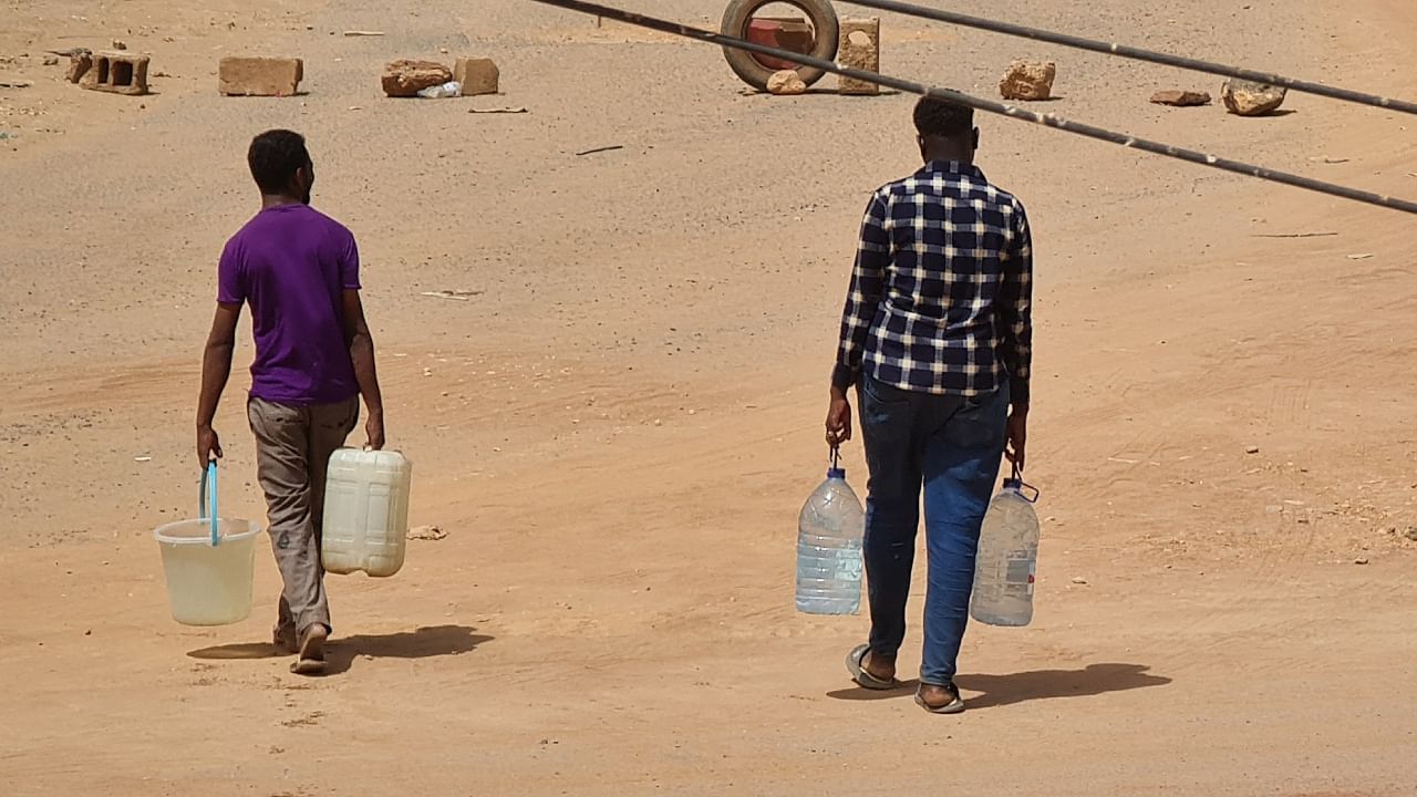 Sudanese men carry bottles of water back to their home in Khartoum on May 25, 2023. Credit: AFP Photo