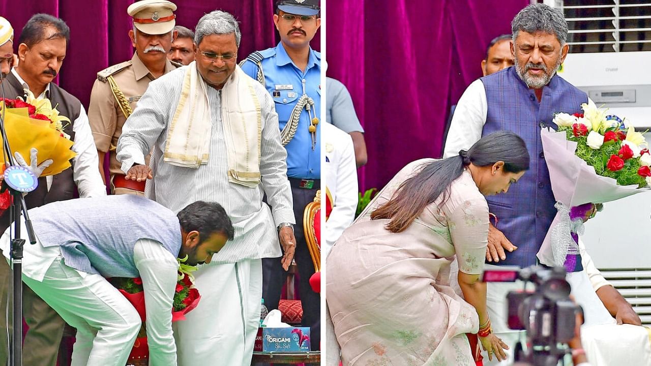 Santosh Lad and Laxmi Hebbalkar prostrate Chief Minister Siddaramaiahand Deputy Chief Minister D K Shivakumar respectively, after taking oath as ministers in Bengaluru on Saturday. Credit: DH Photo/Ranju P