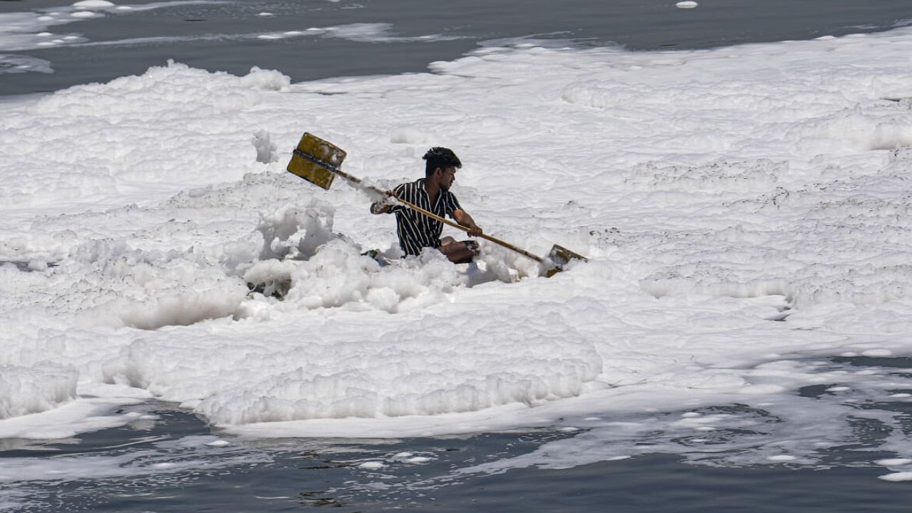 A man rows his makeshift boat through toxic foam covering Yamuna river. Credit: PTI Photo