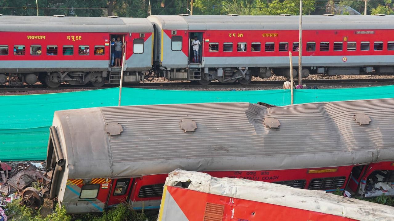 A train runs past derailed coaches after train services resumed on the section where the accident happened on Friday, near Bahanaga Bazar railway station in Balasore. Credit: PTI Photo