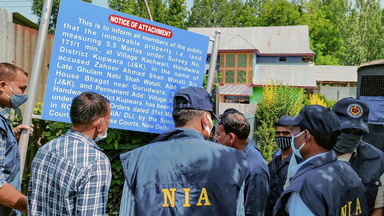 NIA sleuths stand next to a 'notice' mentioning the attachment of Watali's properties. Credit: PTI Photo