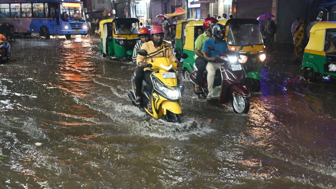 People struggle to reach their destination in heavy rain and rain water flooded on the road at SJP Road in Bengaluru. Credit: DH photo/S K Dinesh