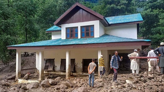 Locals near a damaged house after floods triggered by monsoon rains, in Kahara area of Doda district, Wednesday, July 20, 2022. Credit: PTI File Photo