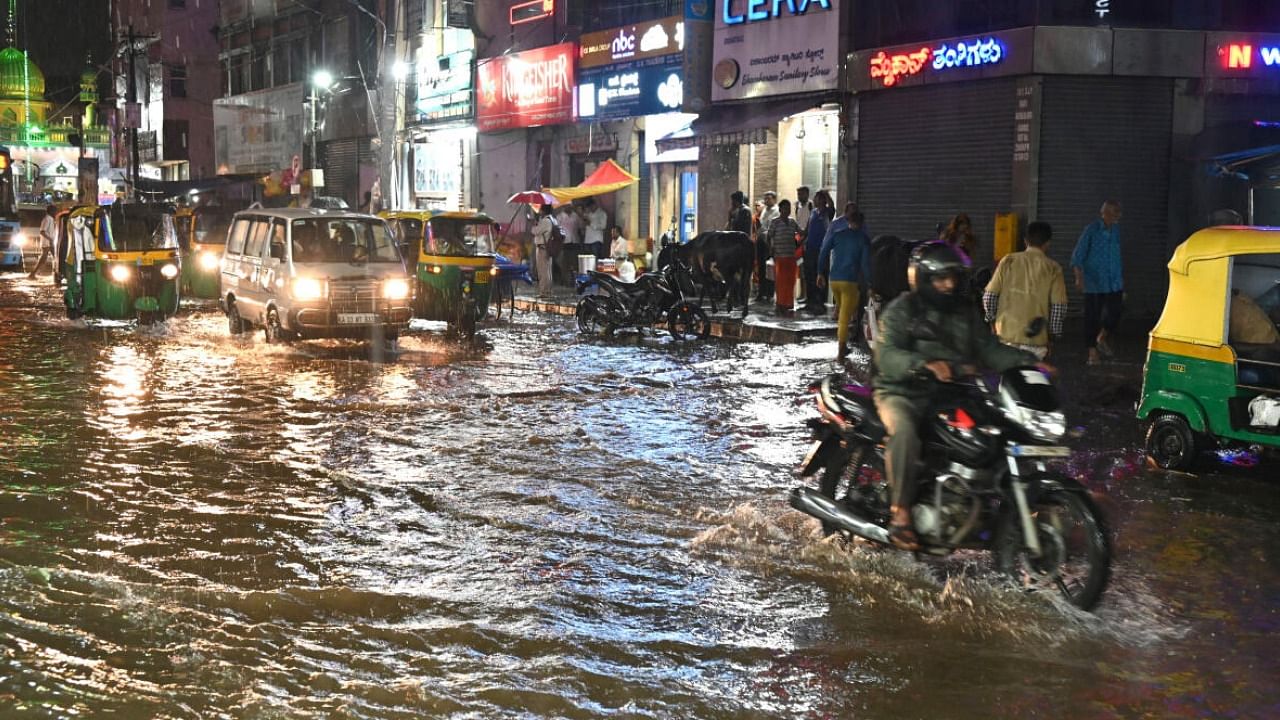 People struggle to reach their destination in heavy rain and rain water flooded on the road at SJP Road in Bengaluru. credit: DH Photo