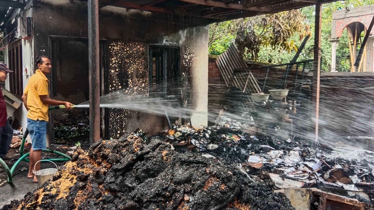 A worker sprays water to cool down burnt items at Union Minister of State for External Affairs R K Ranjan Singh’s residence in Imphal. Credit: PTI Photo