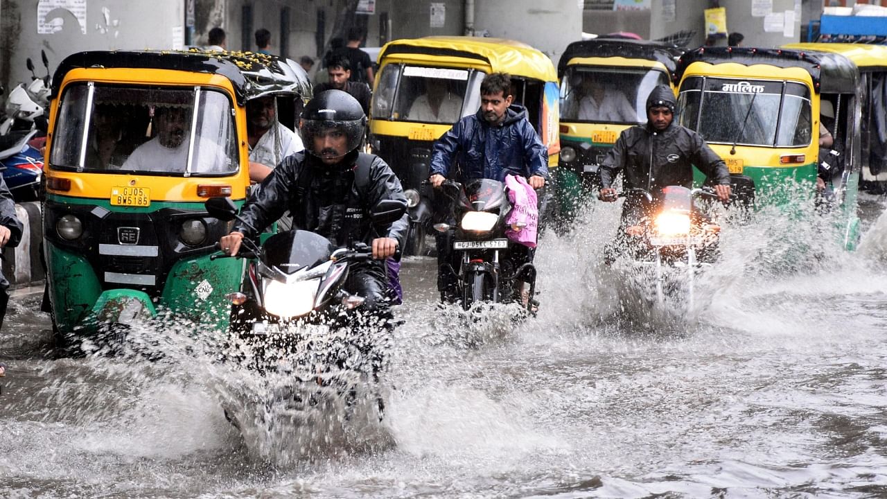 Commuters wade through a waterlogged road following rainfall, in Surat. Credit: PTI File Photo