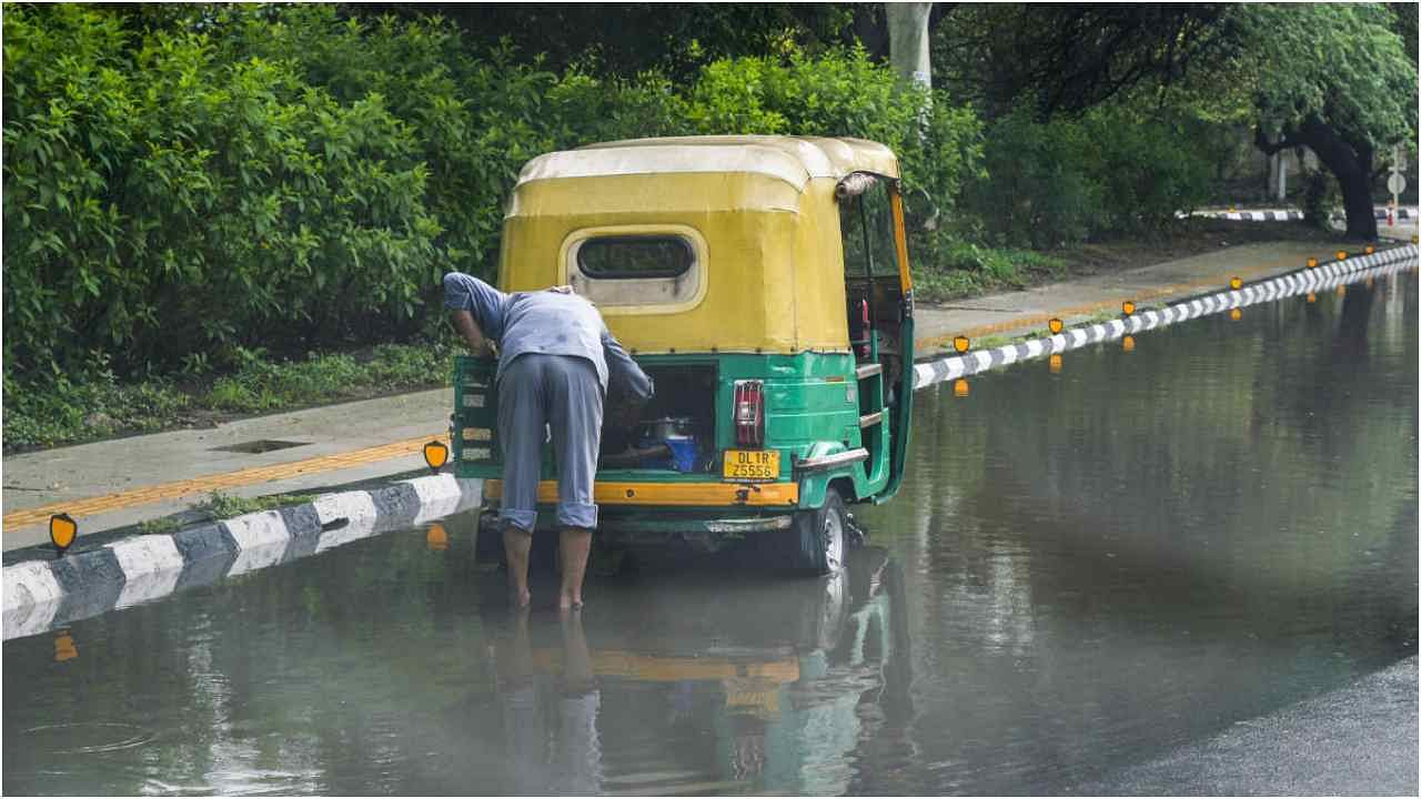 An auto driver checks his auto-rickshaw in the puddle of rainwater as the southwest Monsoon reaches Delhi, Sunday morning, June 25, 2023. Credit: PTI Photo