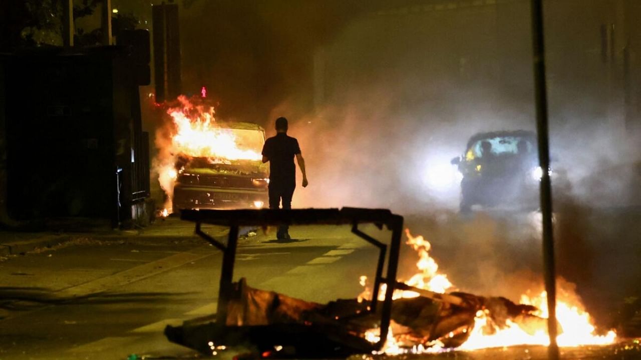 A person stands near a burning vehicle as unrest continues following the death of a 17-year-old teenager killed by a French police officer during a traffic stop, in Nanterre, Paris suburb, France. Credit: Reuters Photo