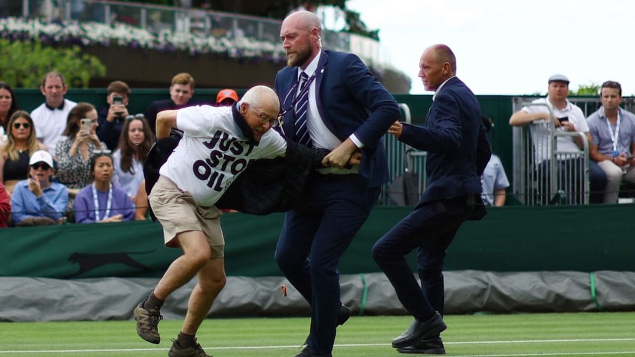 A Just Stop Oil protester is detained by security staff on court 18 during the first round match between Britain's Katie Boulter and Australia's Daria Saville