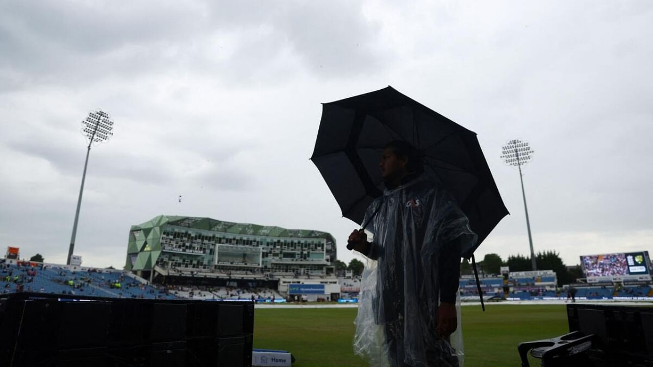 A steward inside the ground holds an umbrella as it rains before the start of play. Credit: Reuters Photo