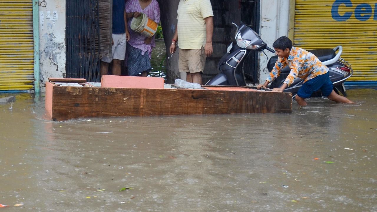 Residents use a wooden slab to prevent rainwater from entering their house during monsoon rain, in Gurugram. Credit: PTI Photo