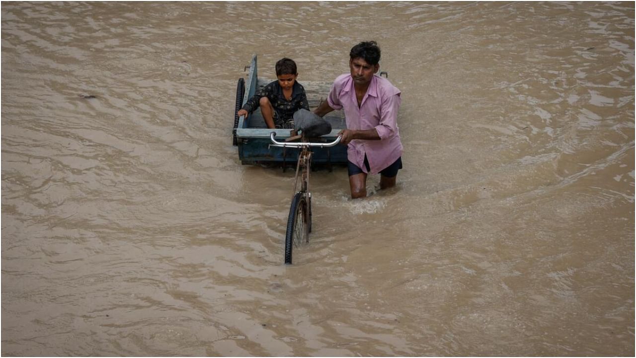 A man carries his son on a rickshaw through a street flooded with the rising water level of river Yamuna after heavy monsoon rains in New Delhi, India, July 12, 2023. Credit: Reuters Photo
