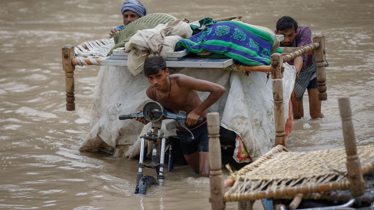 Residents carrying their belongings on a rickshaw as they wade through a street flooded by the rising water level of river Yamuna after heavy monsoon rains in New Delhi, July 12, 2023. Credit: Reuters Photo