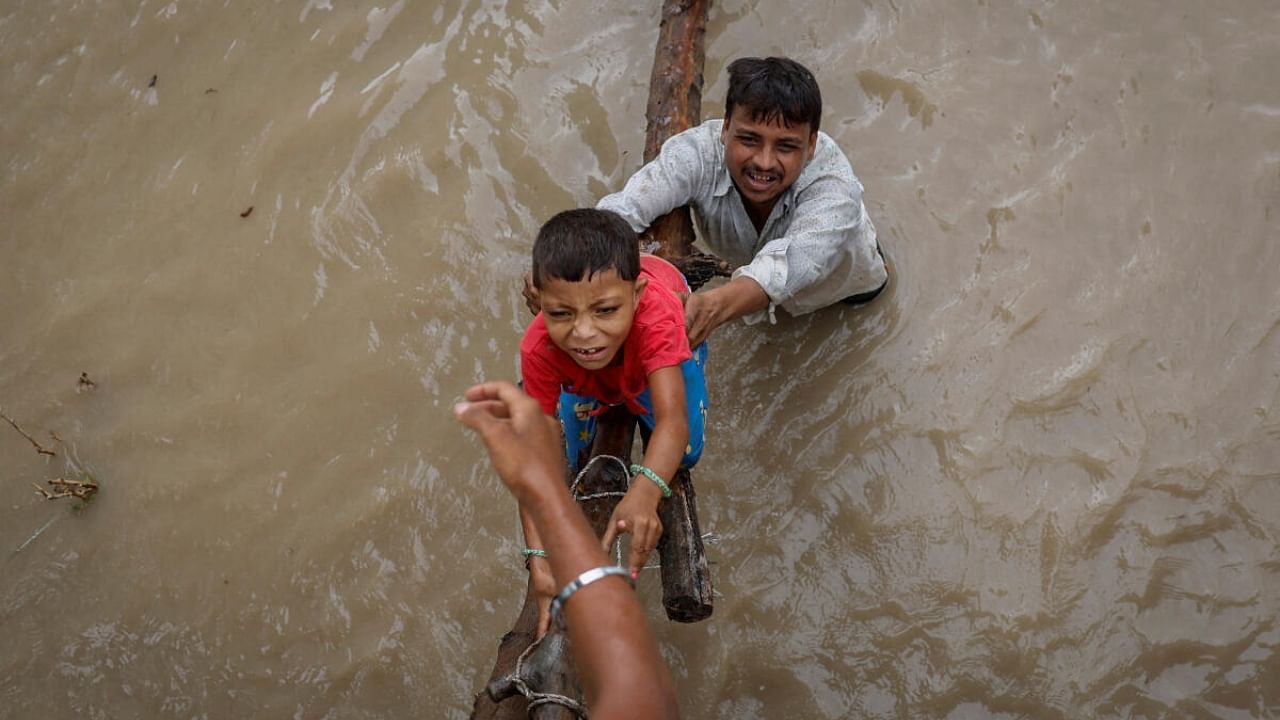 A man helps his son to climb onto a flyover under construction, after being displaced by the rising water level of river Yamuna after heavy monsoon rains in New Delhi, India, July 12, 2023. Credit: Reuters Photo