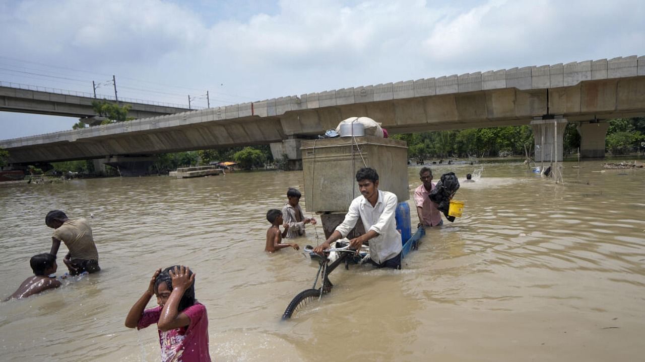 People from low-lying areas carry their belongings while relocating to a safer place after the Yamuna river inundated the nearby areas. Credit: PTI Photo