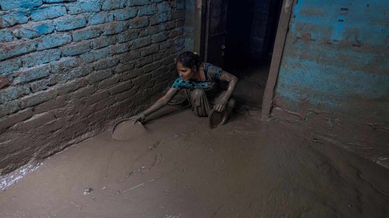 Delhi woman cleans the mud from the entrance of her house as flood water recedes. Credit: Reuters Photo