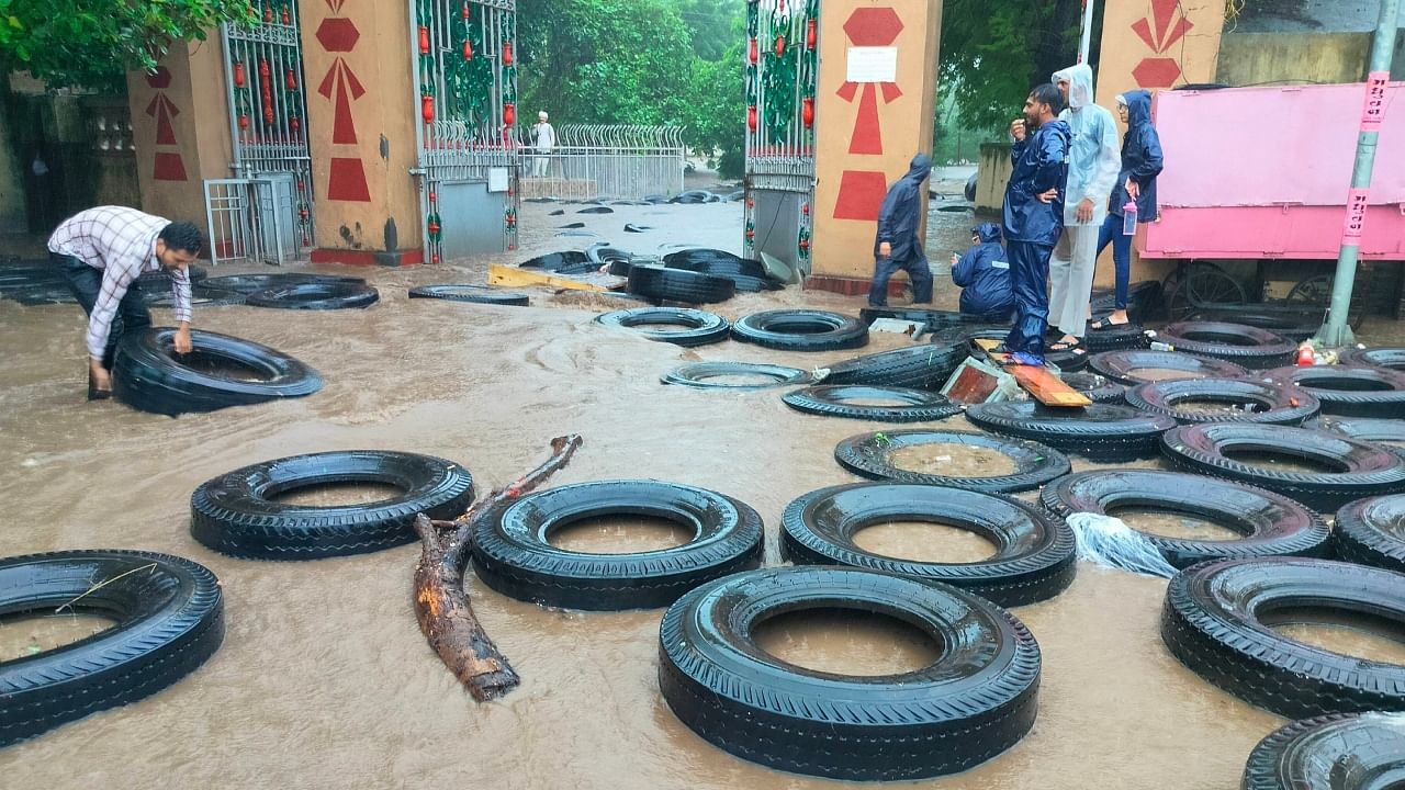 A man places tyres in an inundated area after heavy rainfall triggered a flood-like situation in Junagadh district, Saturday, July 22, 2023. Credit: PTI Photo