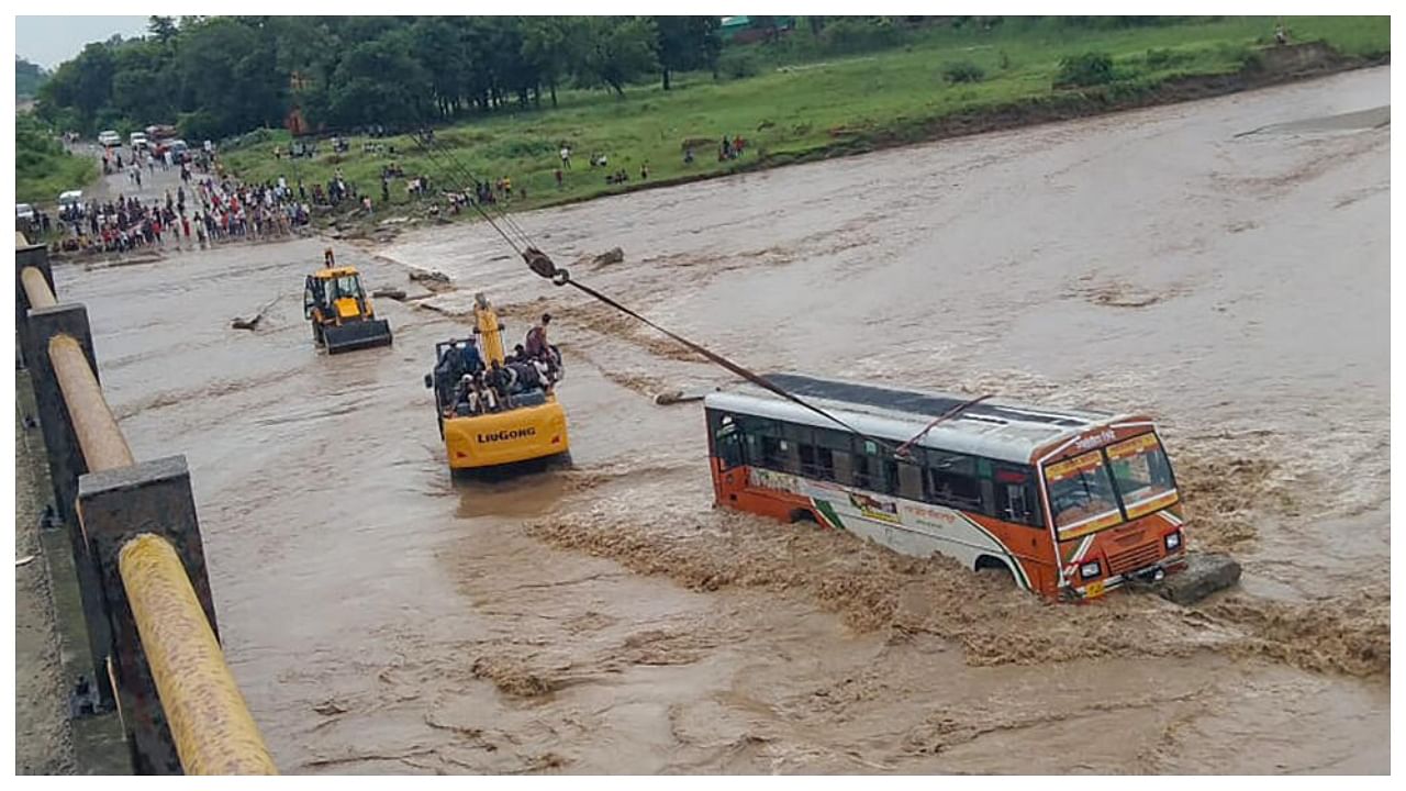 An earthmover helps rescue a Uttar Pradesh State Road Transport Corporation bus that got stuck in the strong water current of the Kotawali river at Mandawali area, in Bijnor district, Saturday, July 22, 2023. Credit: PTI Photo