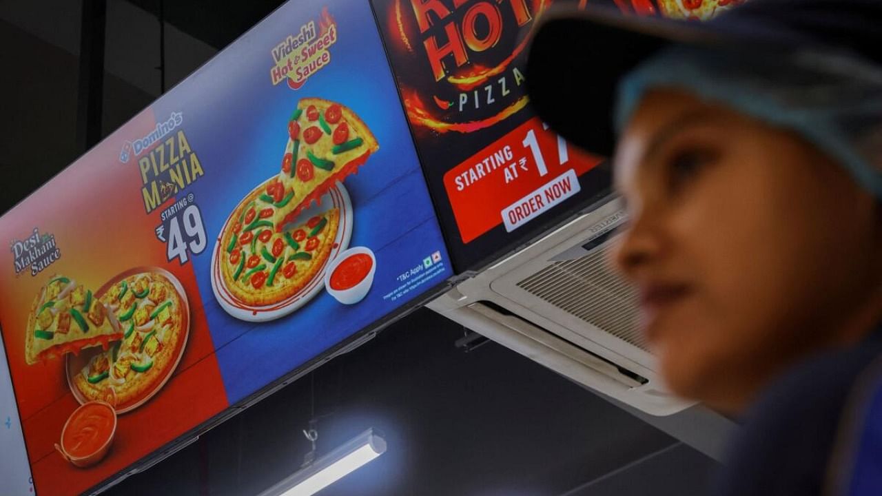 A Domino's staff member stands next to a sign for a Rs 49 pizza at a restaurant in Noida, India, July 4, 2023. Credit: Reuters Photo