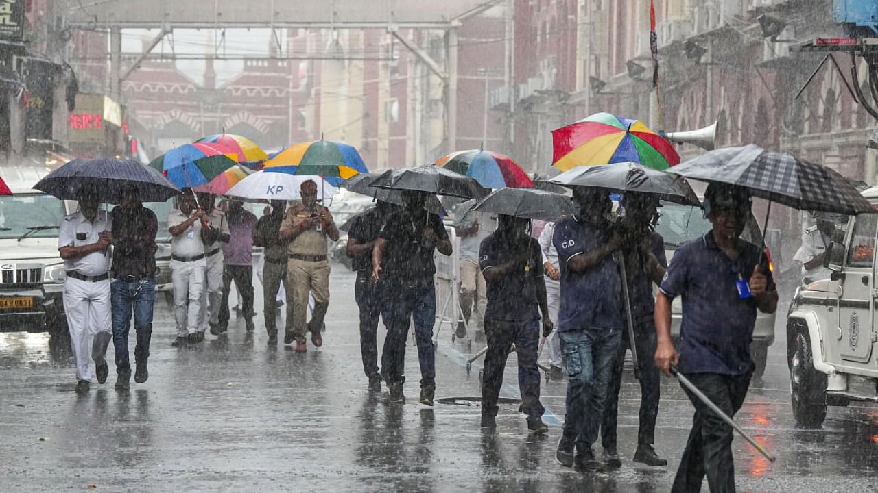 Police personnel hold umbrellas amid rains as they perform their duty, in Kolkata. Credit: PTI Photo