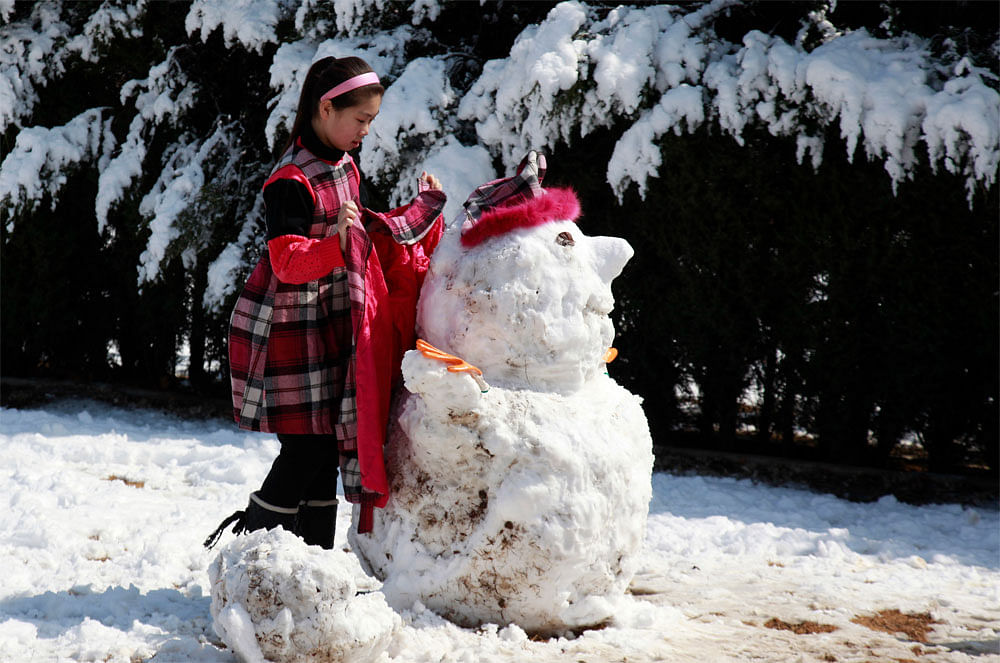 A Chinese girl dresses up a snow man after overnight snow capped the  Chinese capital in white in Beijing, China, Sunday, March 18, 2012.AP Photo