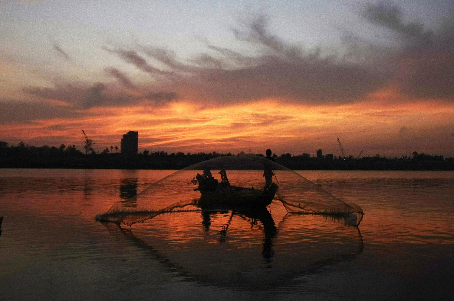 A Cambodian fisherman throws his fishing net in the morning from a wooden boat at Tonle Sap river in Phnom Penh, Cambodia. AP