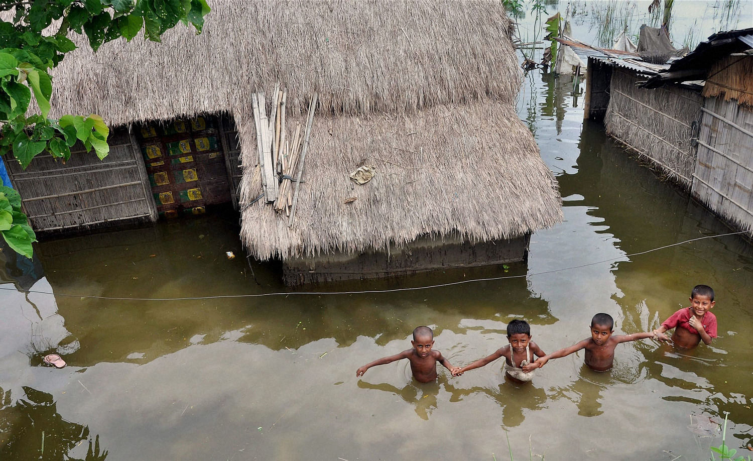 Children wade through water at Burabure near Moriagaon on Sunday. Heavy rainfall has flooded many villages in the Moriagaon district. PTI