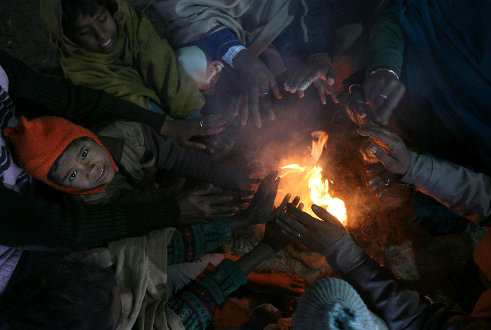 People warm themselves by a fire at a pavement on a cold winter morning in the northern Indian city of Chandigarh January 6, 2013. The coldest weather in northern India has killed more than 100 homeless people, an aid group said last week. Temperatur...