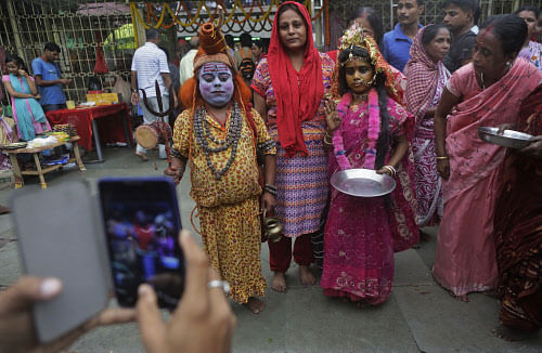 A devotee takes photographs on his mobile phone as his wife poses with a man dressed as god Shiva and a girl dressed like goddess Parvati during the Ambubasi festival at the Kamakhya temple in Gauhati, Sunday, June 22, 2014. The annual festival where...