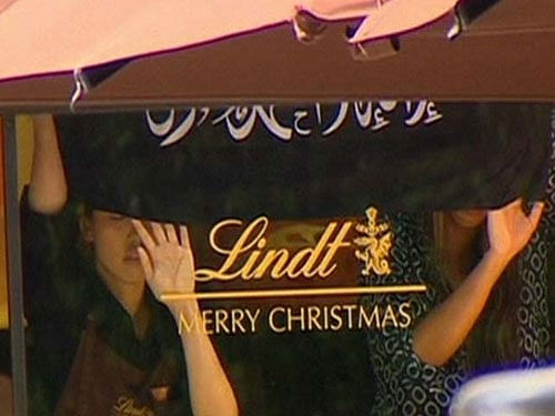 People holding up what appeared to be a black flag with white Arabic writing on it, inside a cafe in Sydney. Several people were today taken hostage at a popular cafe in Sydney apparently by at least one Islamic State gunman, media reports said. AP p...