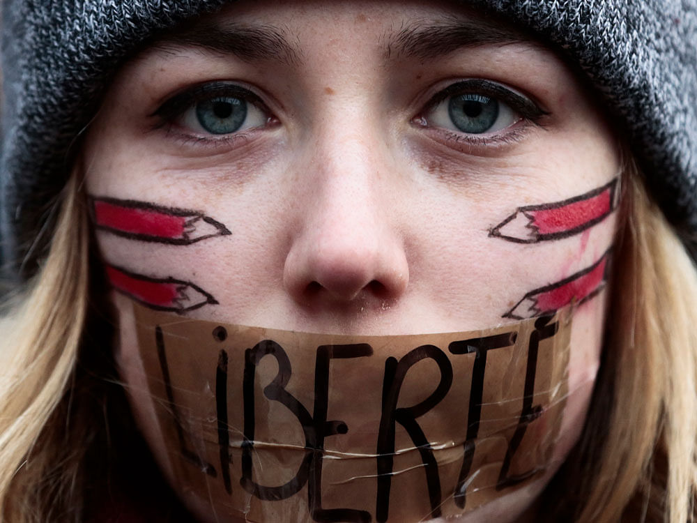 A woman with her mouth taped displaying the word freedom,gathers with several thousand people in Berlin to honor the 17 victims who died during three days of bloodshed in Paris last week, and to support freedom of expression. AP Photo.
