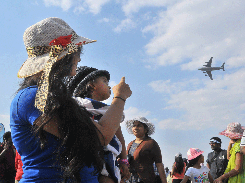 A lady showing flaying US aircraft to her kid during the Aero India 2015 at Yelahanka Airbase in Bengaluru on Saturday. DH Photo.