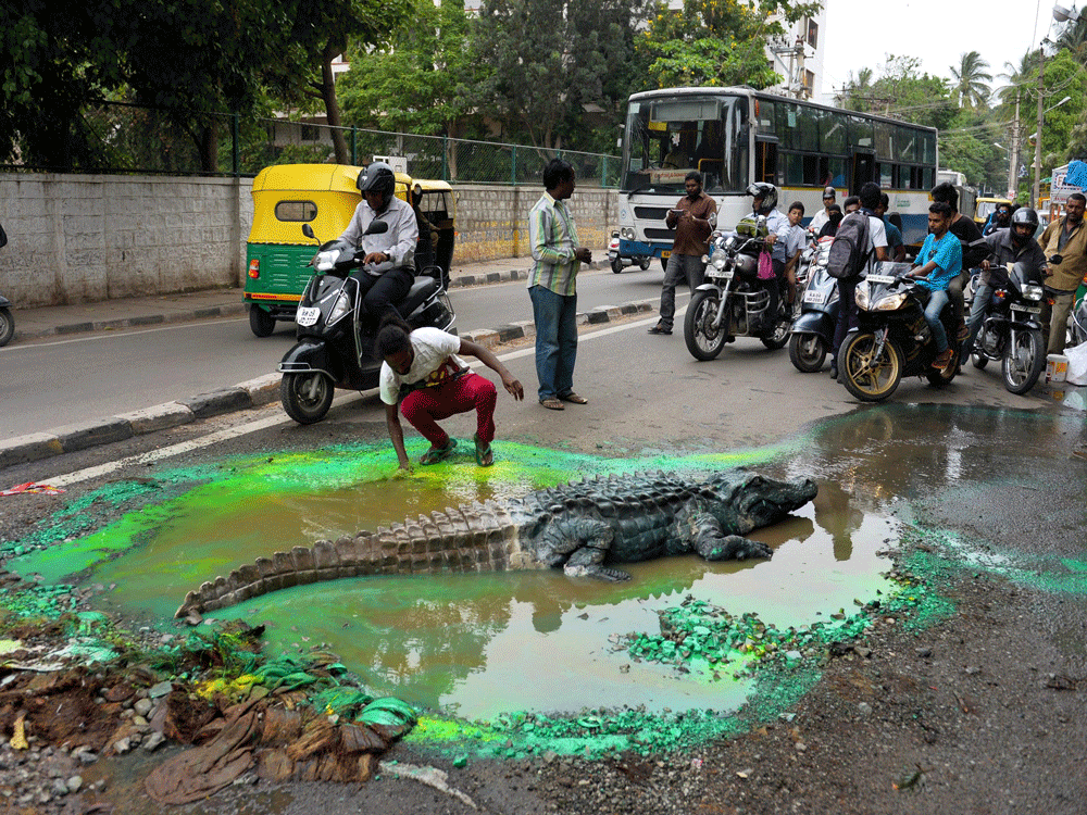 Baadal Nanjundaswamy, an artist from Bengaluru creates a temporary art  installation with a model of a crocodile sitting inside a big pot hole  posing problems for commuters, to draw attention of the Bruhat Bengaluru  Mahanagara Palike on Sultanpalya...
