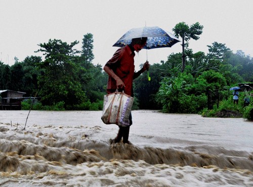  An elderly man wades through a submerged bridge in flood water at Bengalipara in Baska district of Assam on Sunday. PTI Photo