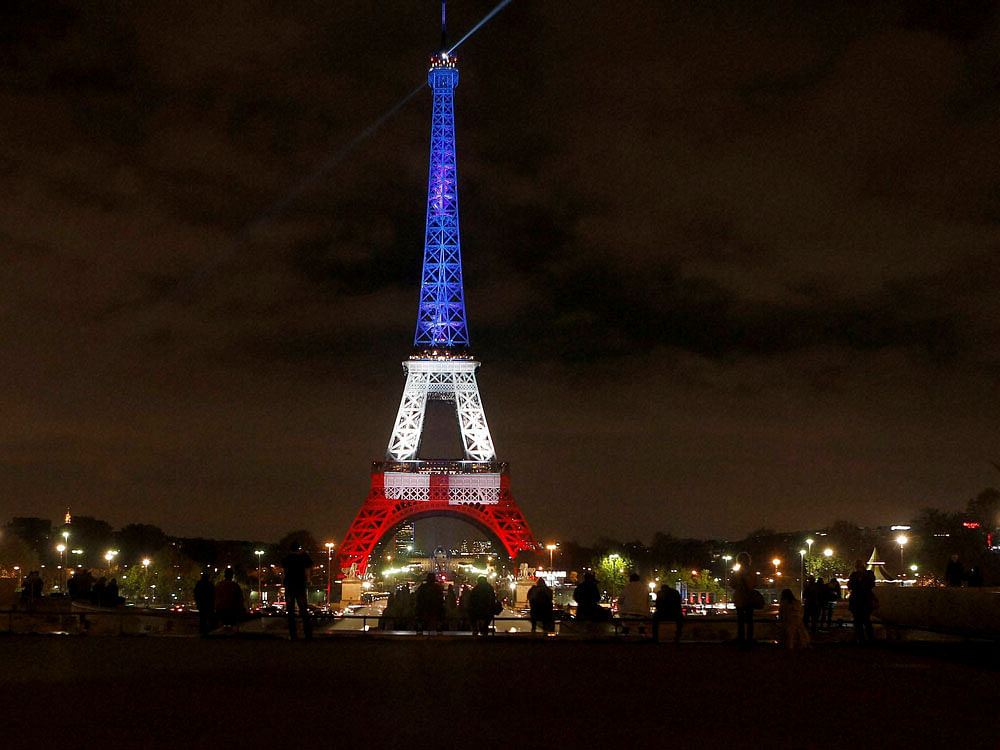  People look at the Eiffel Tower illuminated in the French colors in honor of the victims of the attacks on Friday in Paris, Monday, Nov. 16, 2015. AP/ PTI