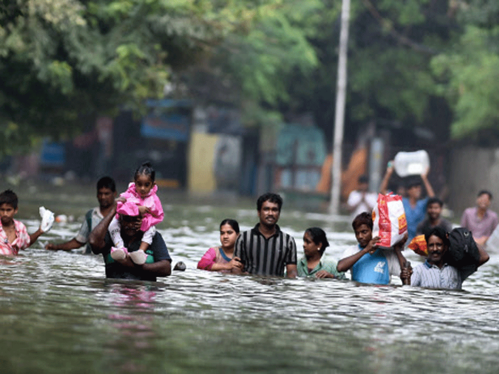 People wade through flood waters  in rain-hit Chennai on Thursday. PTI Photo