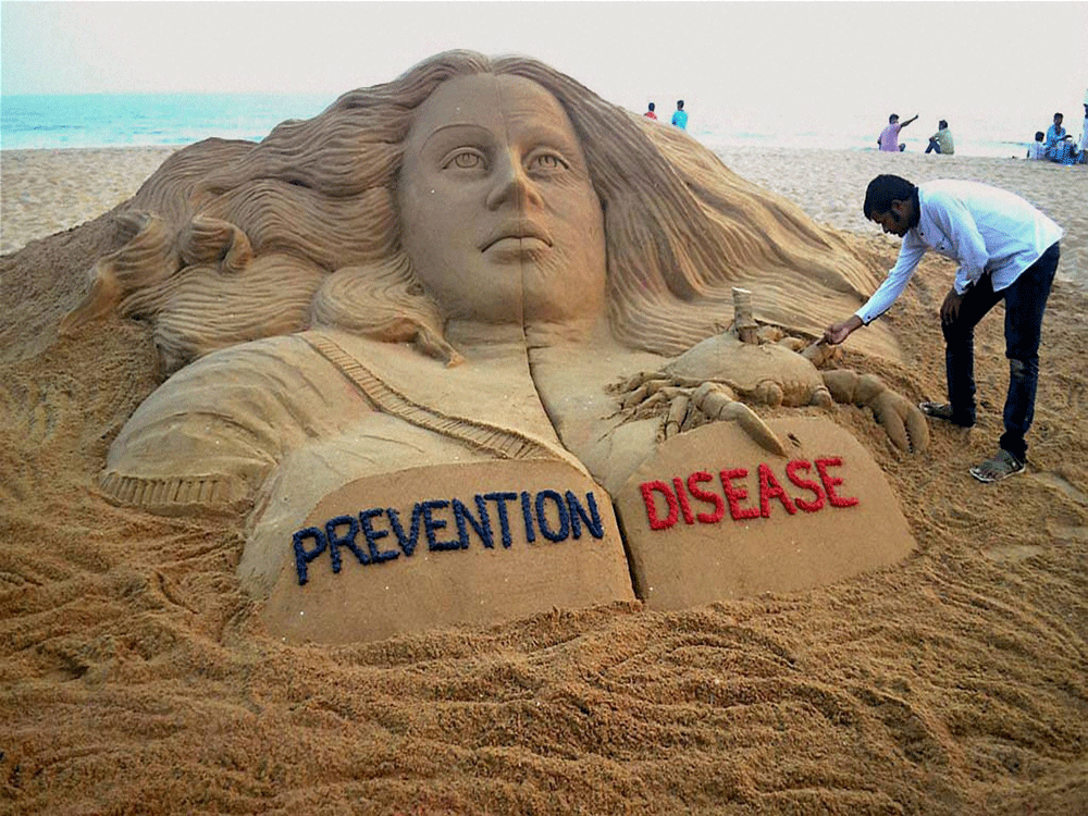 Sand artist Sudarsan Pattnaik spreading awareness against breast cancer through his sand sculpture with message 'prevention vs disease' at Puri beach on Saturday. PTI Photo.