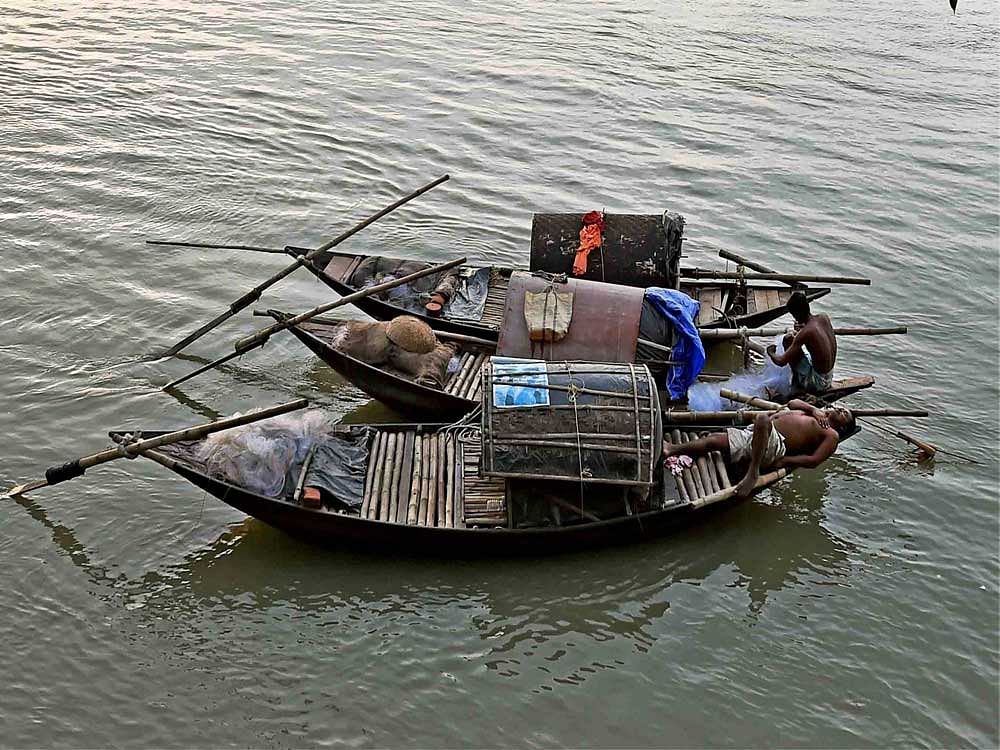 A fisherman takes nap on a boat while another busy with nets on the river Ganga in Kolkata on Thursday afternoon. PTI