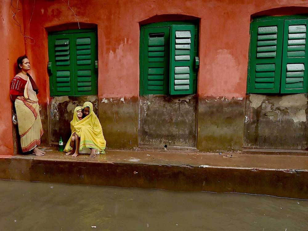 Passers-by take shelter under the balcony of a house during heavy rainfall in Kolkata on Monday. PTI Photo