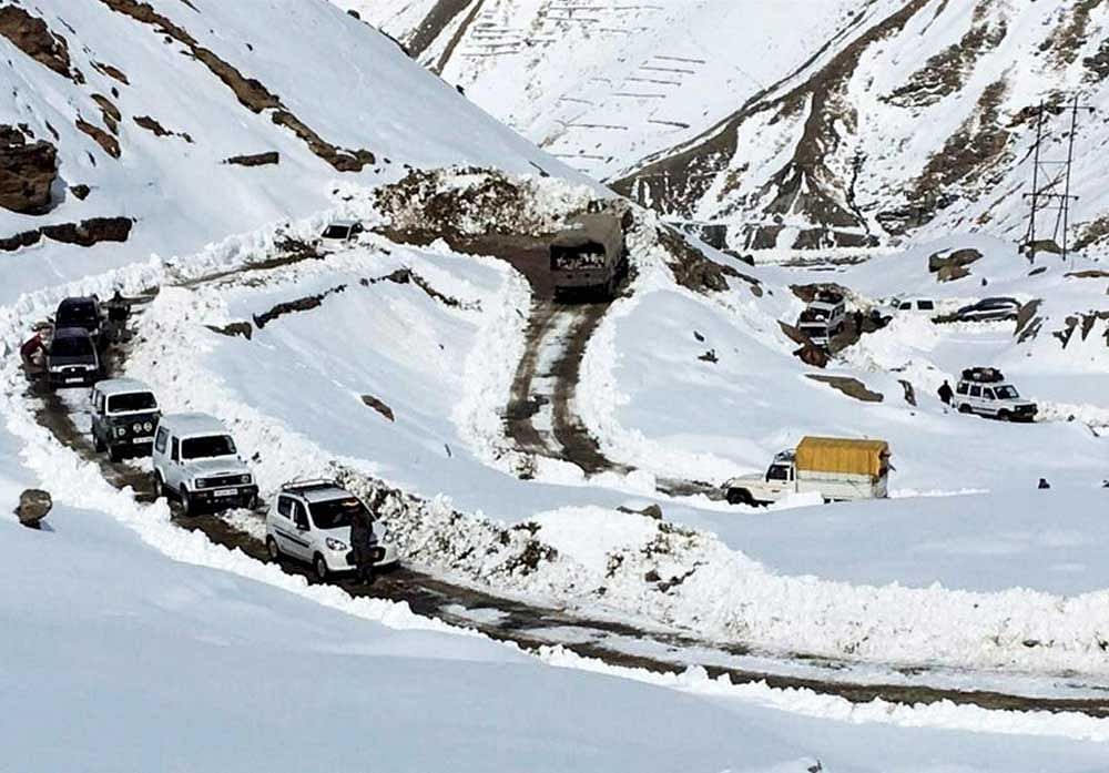 Vehicles moving at snow clad road after snowfall in Lahau. PTI Photo