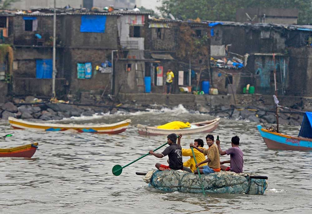 Fishermen move through the rough sea to cover thier boats as it rains in Mumbai on Tuesday. PTI