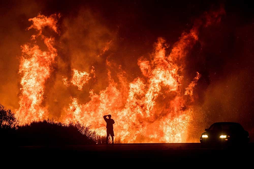 A motorists on Highway 101 watches flames from the Thomas fire leap above the roadway north of Ventura, Calif., on Wednesday, Dec. 6, 2017. As many as five fires have closed highways, schools and museums, shut down production of TV series and cast a ...