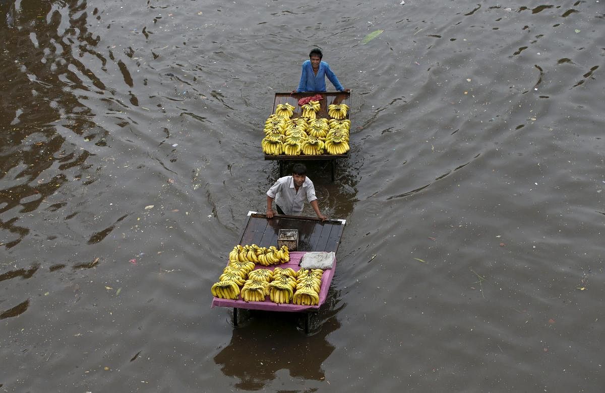 Fruit vendors pass through a flooded street after heavy rains, in Ahmedabad on Sunday, June 24, 2018. PTI
