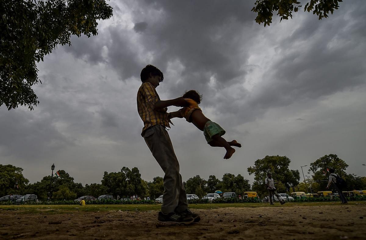 A young boy plays with a child as pre-monsoon clouds gather in the sky, in New Delhi, on Tuesday, June 26, 2018. PTI