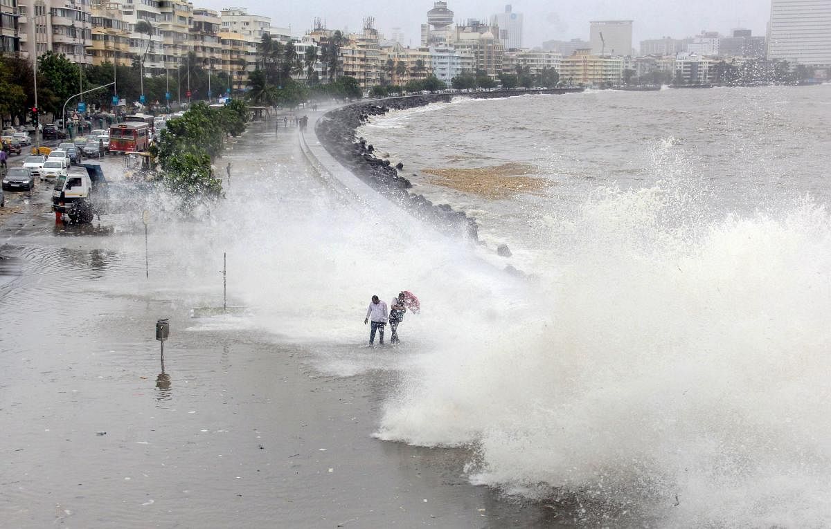 People walk along the shore as a high tide hits the sea wall at Marine Drive, in Mumbai on Saturday, 14 July 2018. (PTI Photo)
