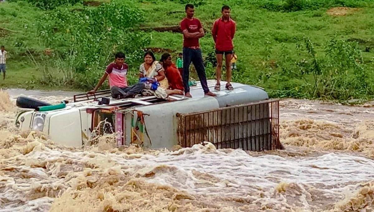 People stand atop vehicle that collapsed into flooded water following heavy monsoon rains, in Latehar on Monday, Sept 3, 2018. (PTI Photo)