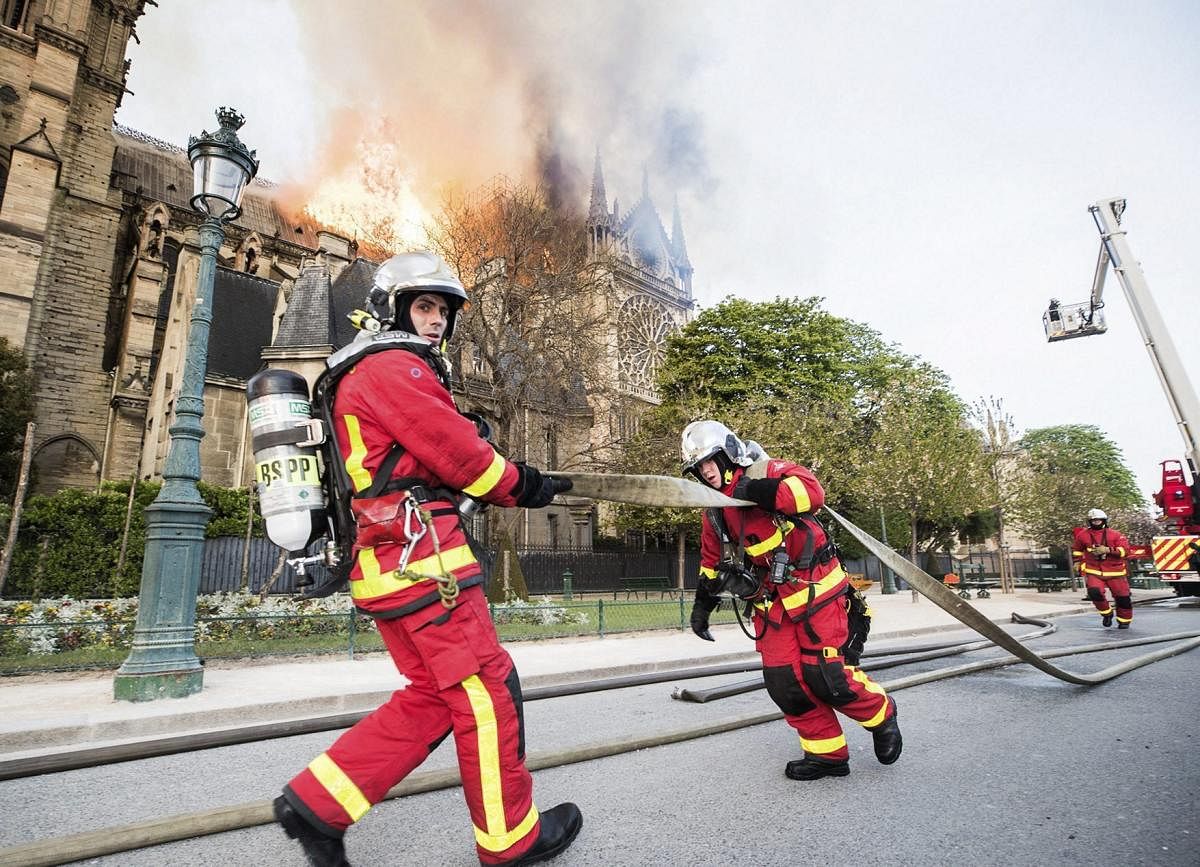 This photo provided Tuesday April 16, 2019 by the Paris Fire Brigade shows fire fighters pulling a hose by the burning Notre Dame cathedral, Monday April 15, 2019. Experts assessed the blackened shell of Paris' iconic Notre Dame Tuesday morning to establish next steps to save what remains after a devastating fire destroyed much of the cathedral that had survived almost 900 years of history. AP/PTI