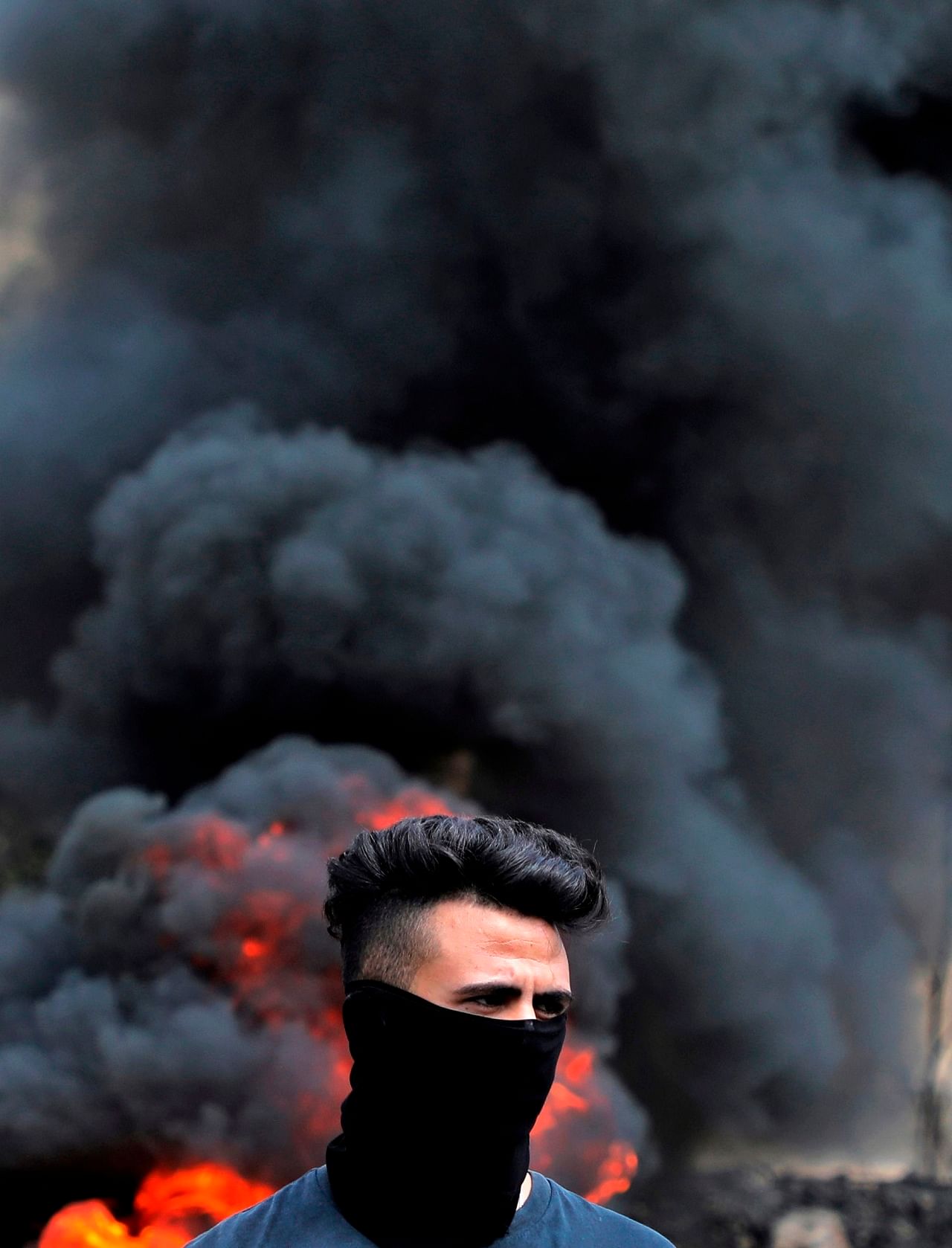 A Palestinian demonstrator stands in front of burning tyres during clashes following a weekly protest against the expropriation of Palestinian land by Israel